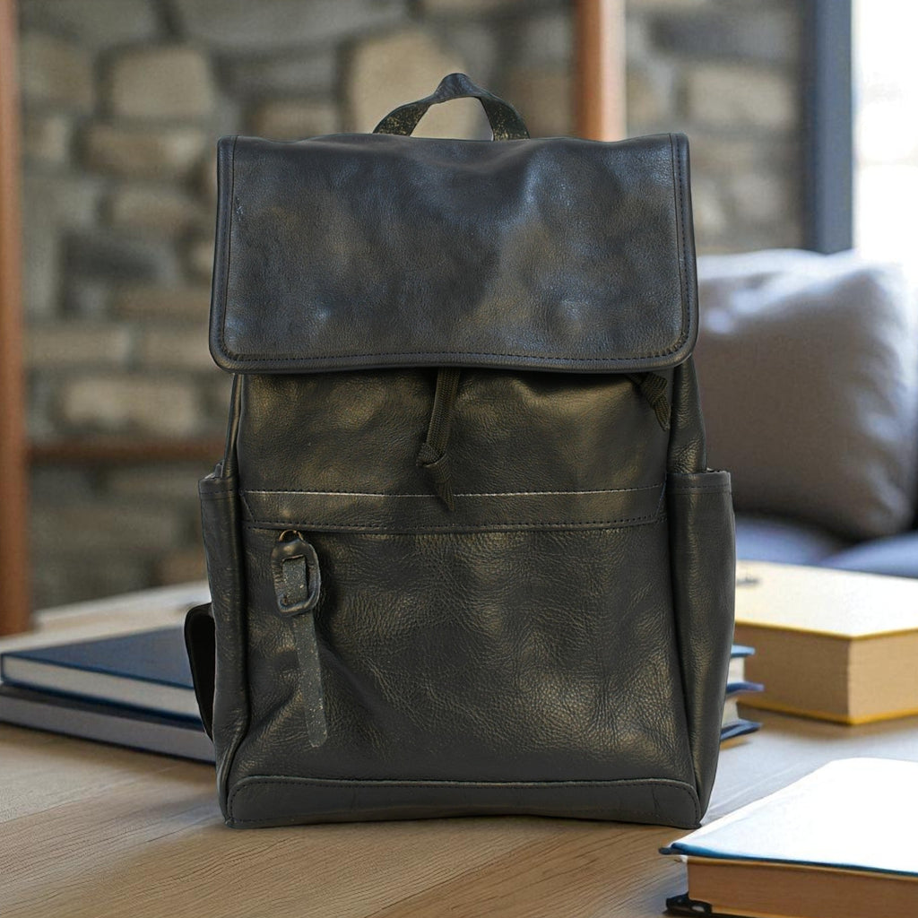 Dark leather modern rugged backpack on a wooden surface with books and a stone wall background