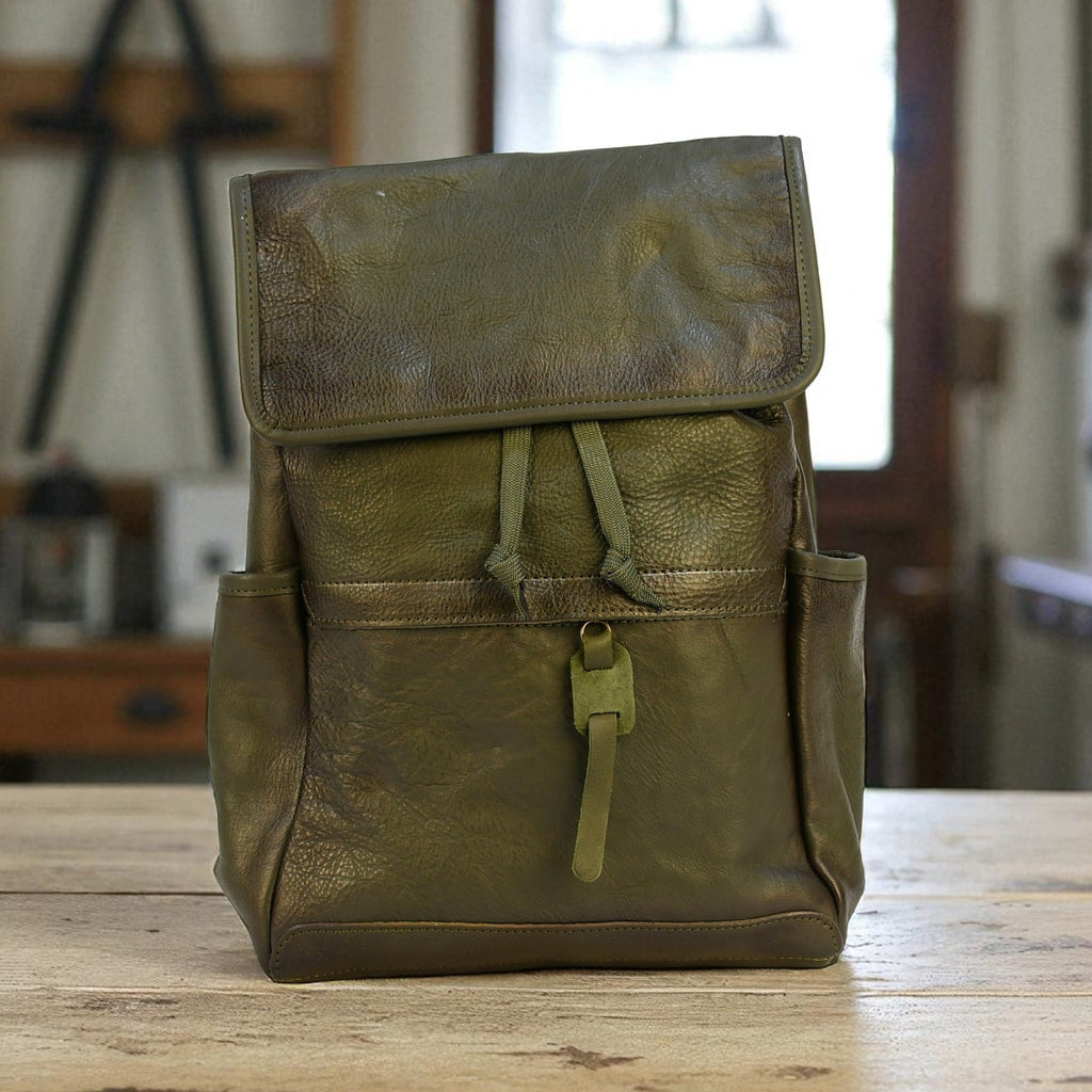 Green leather modern rugged backpack on a wooden table with a blurred indoor background