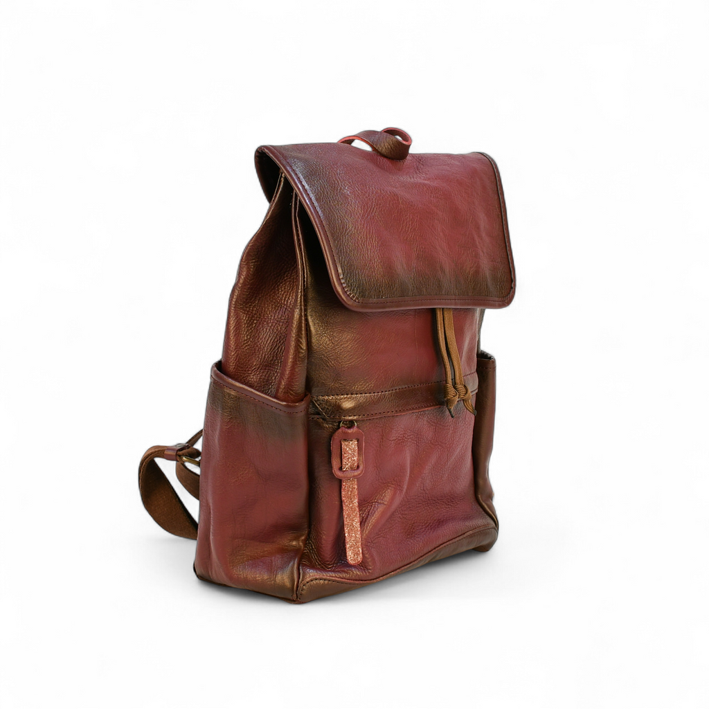 Purple modern rugged leather backpack on a rocky outcrop with a mountainous landscape and sunset in the background