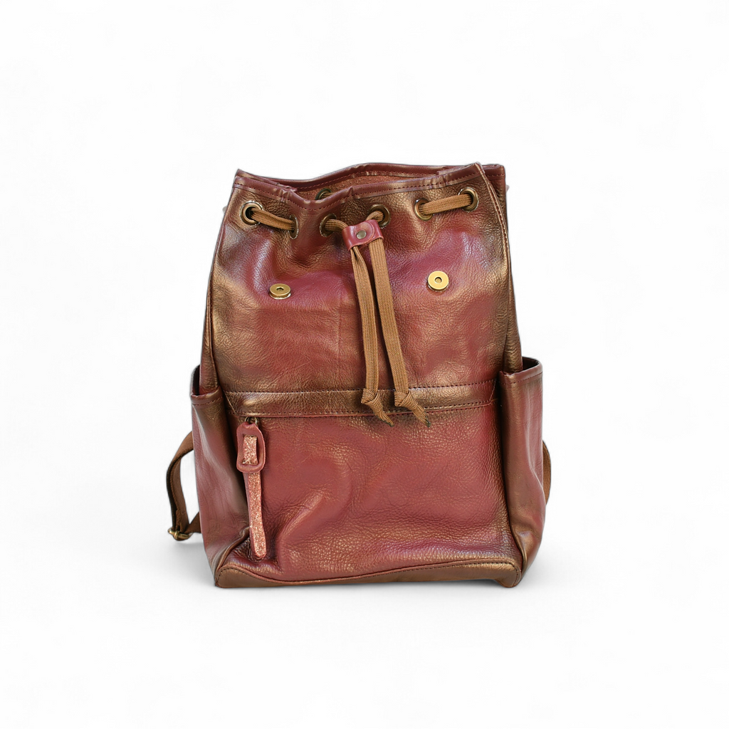 Purple modern rugged leather backpack on a rocky outcrop with a mountainous landscape and sunset in the background