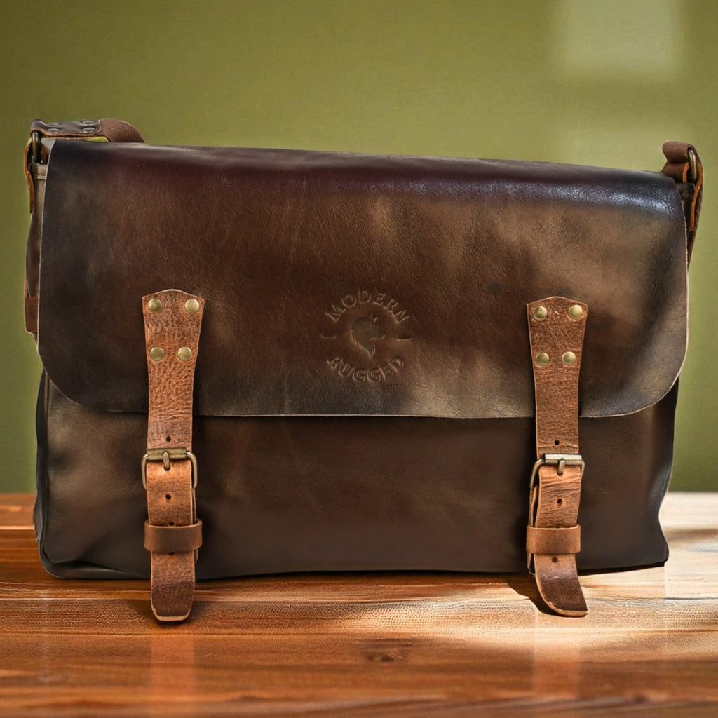 Brown leather bag with gold buckles on a wooden surface against a green wall.