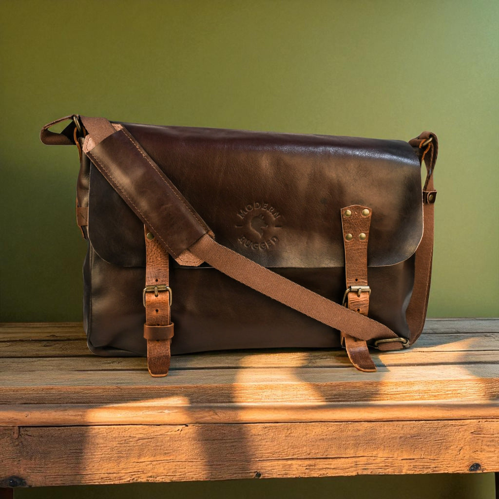 Brown leather bag with a strap on a wooden surface against a green wall