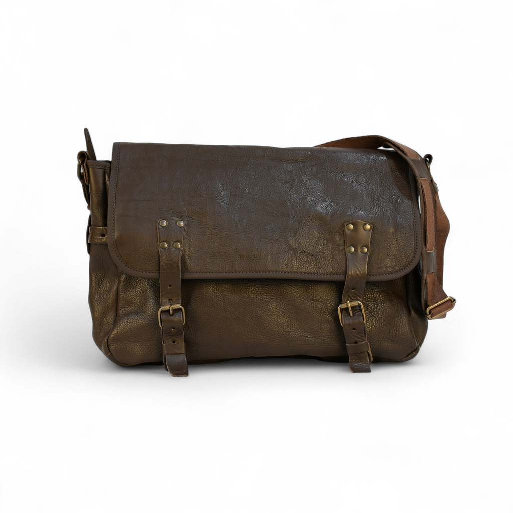 Brown leather modern rugged messenger bag on a forest floor with trees and foliage in the background