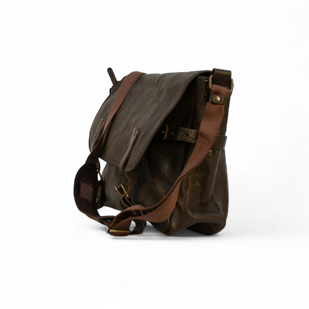 Brown leather modern rugged messenger bag on a forest floor with trees and foliage in the background