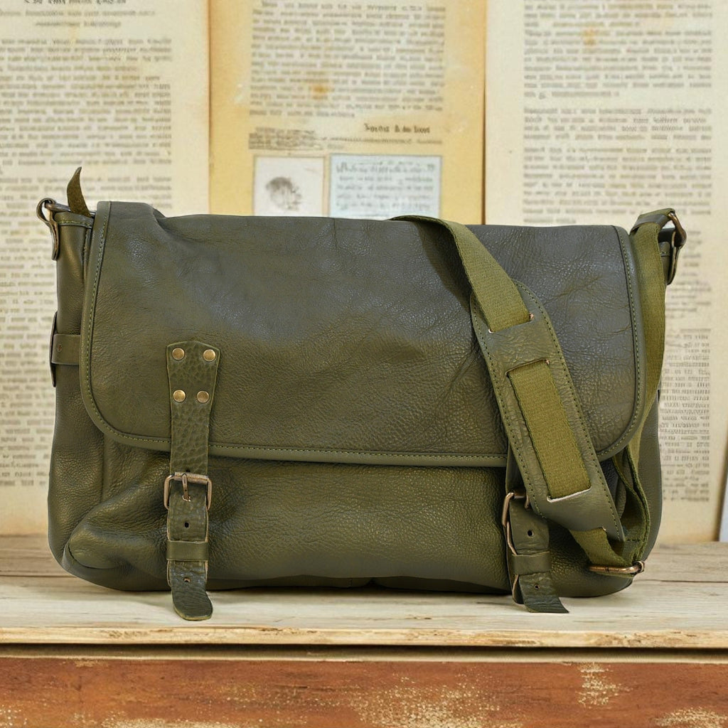 Green leather modern rugged messenger bag on a wooden surface with vintage books in the background