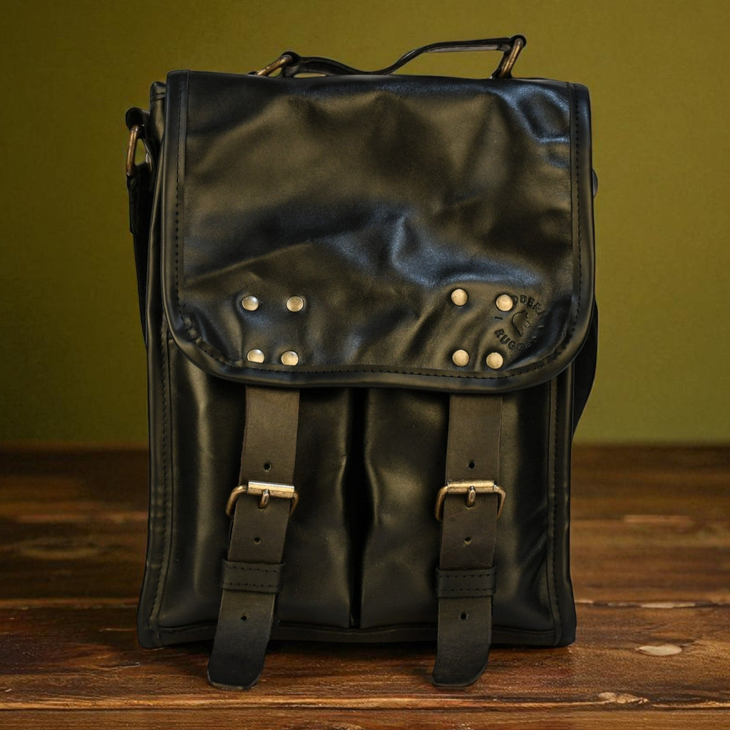 Black modern rugged leather backpack with studs on a wooden surface and green background