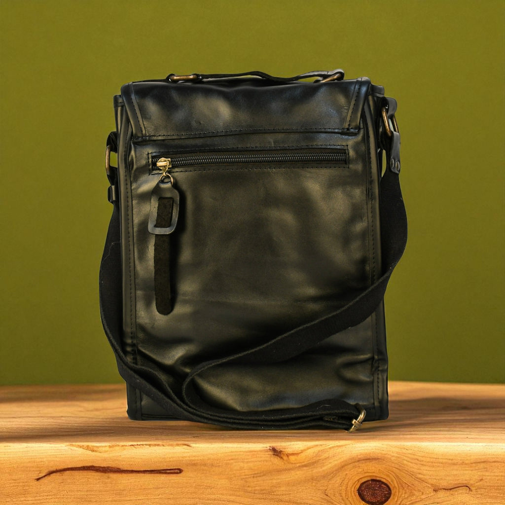 Black modern rugged leather backpack with studs on a wooden surface and green background