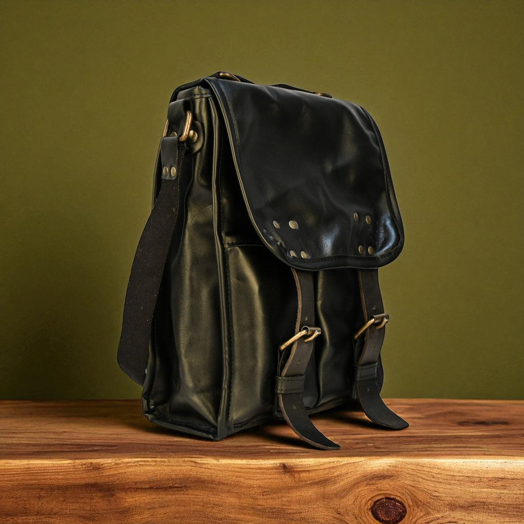 Black modern rugged leather backpack with studs on a wooden surface and green background