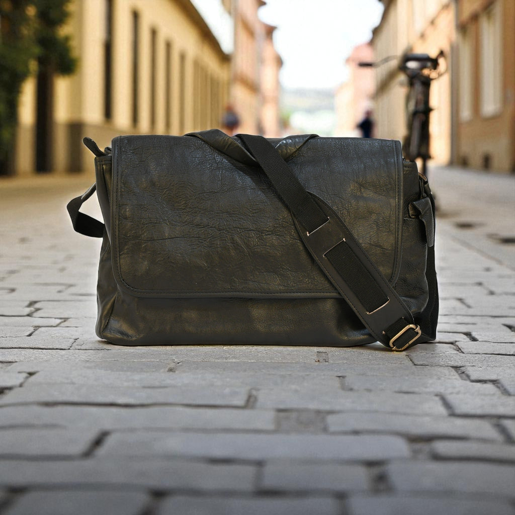Black modern rugged leather bag with a black strap on a stone pavement street.