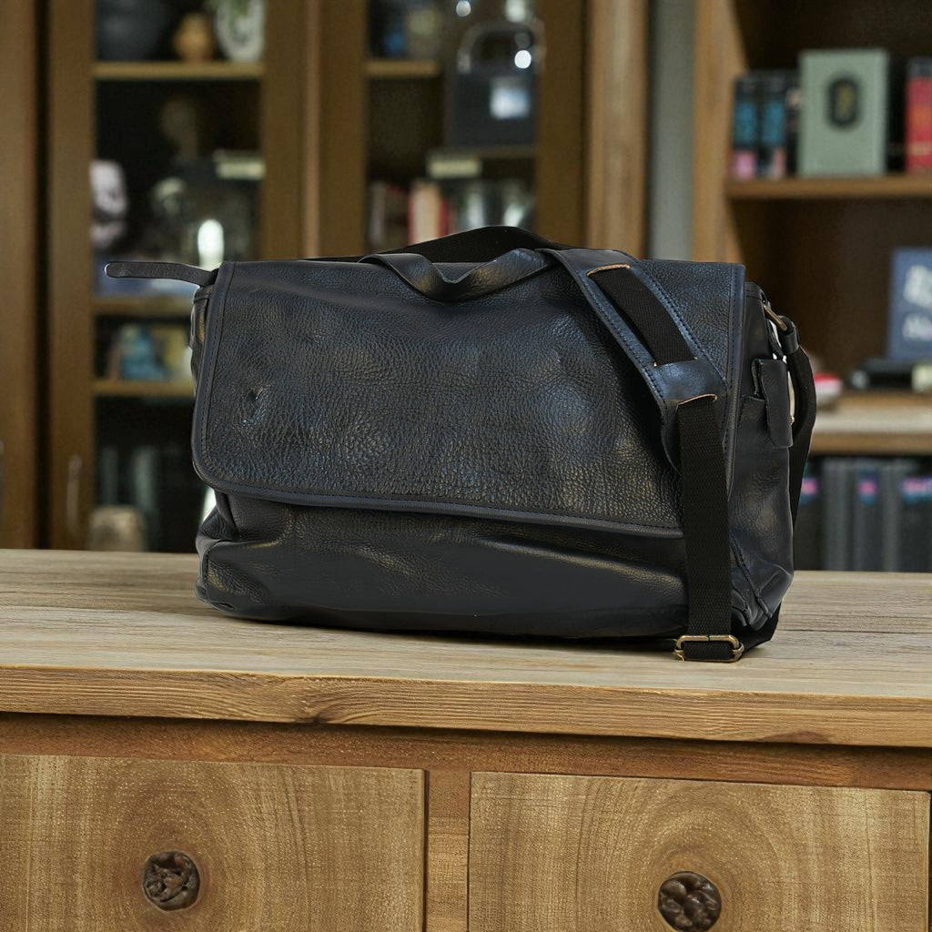 Black modern rugged leather bag with a black strap on a stone pavement street.
