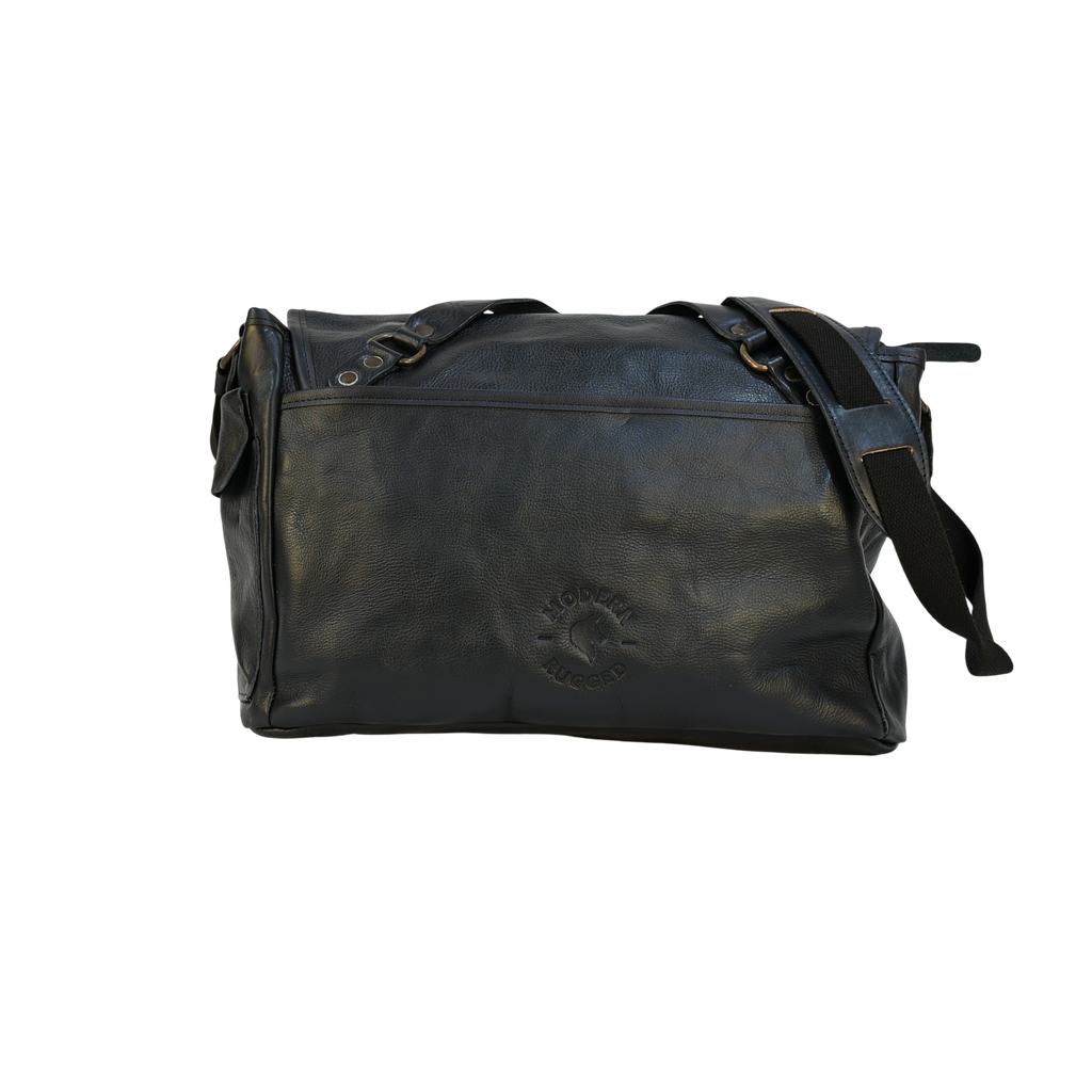 Black leather modern rugged messenger bag on a wooden table with a gray background