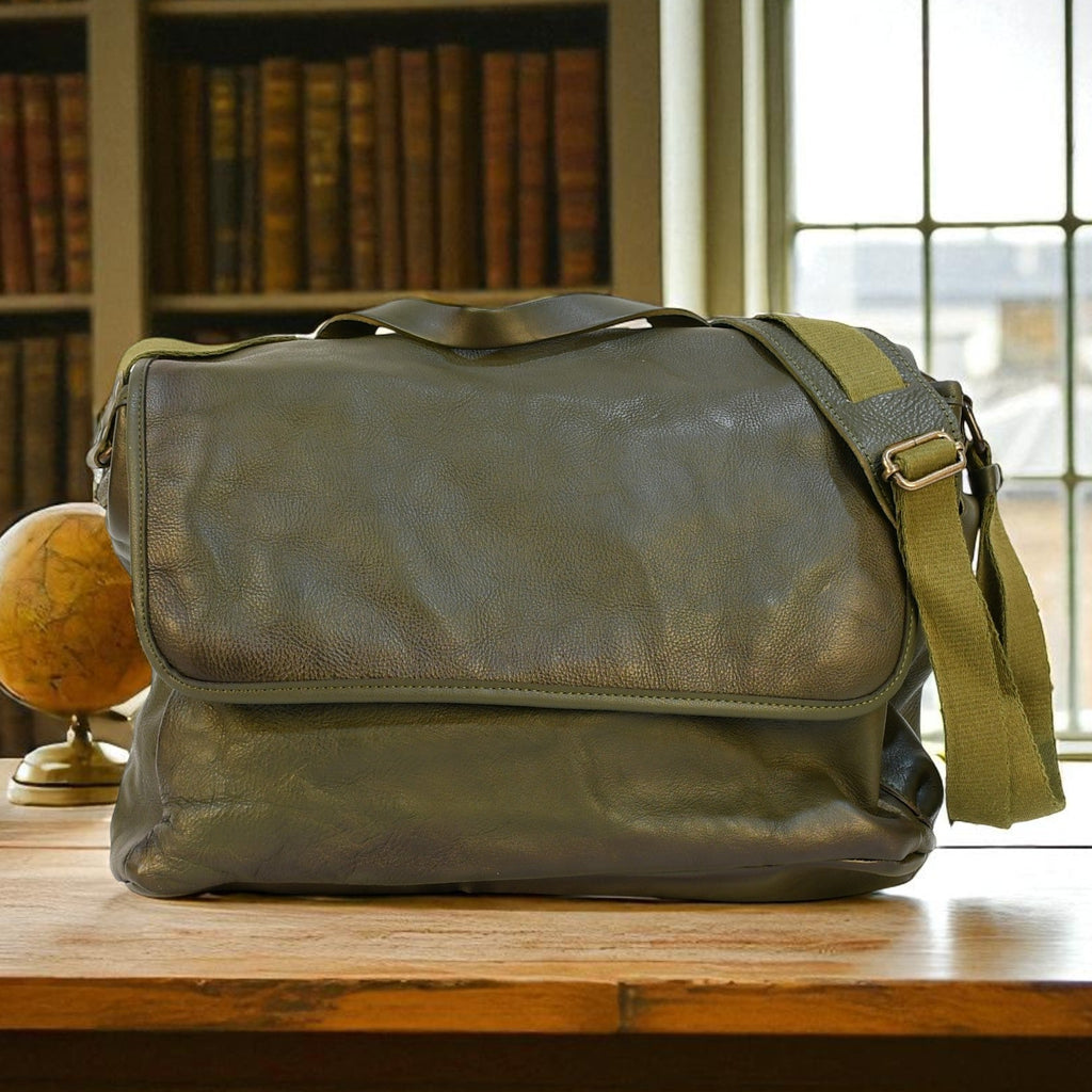 Green modern rugged leather bag on a wooden desk with bookshelves and a window in the background