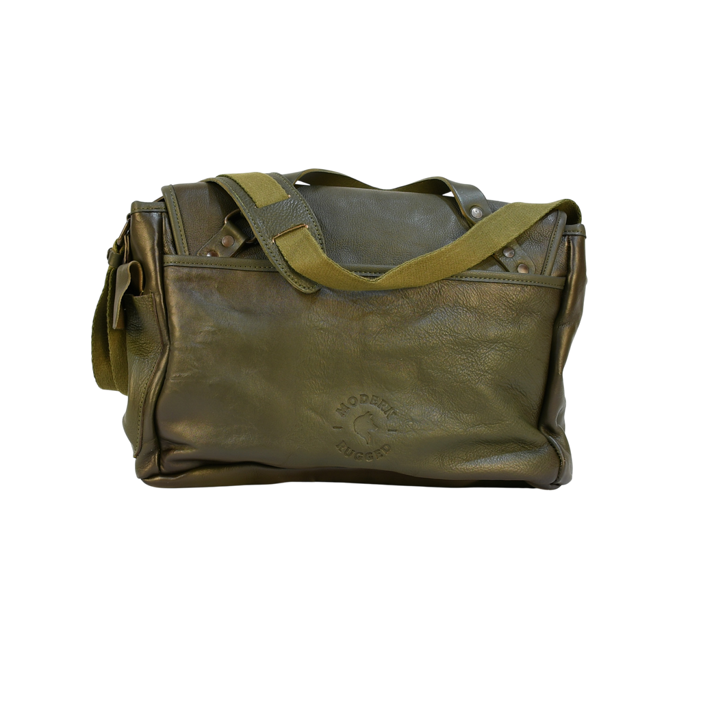 Green modern rugged leather bag on a wooden desk with bookshelves and a window in the background