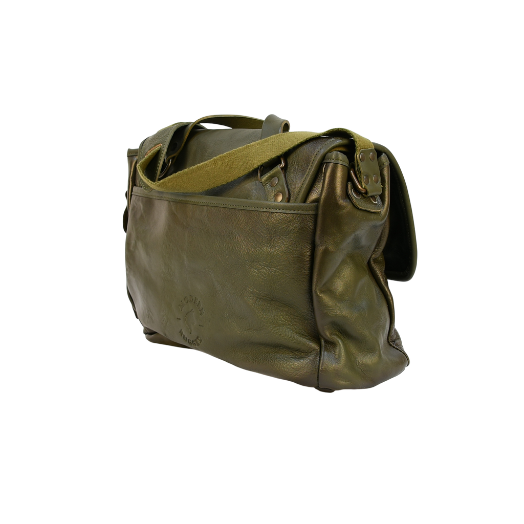 Green modern rugged leather bag on a wooden desk with bookshelves and a window in the background