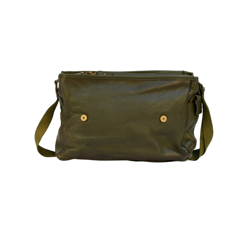 Green modern rugged leather bag on a wooden desk with bookshelves and a window in the background