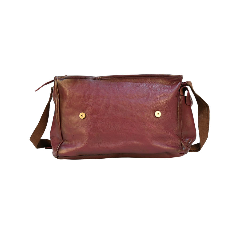 purple modern rugged leather bag on a wooden table with a bookshelf in the background