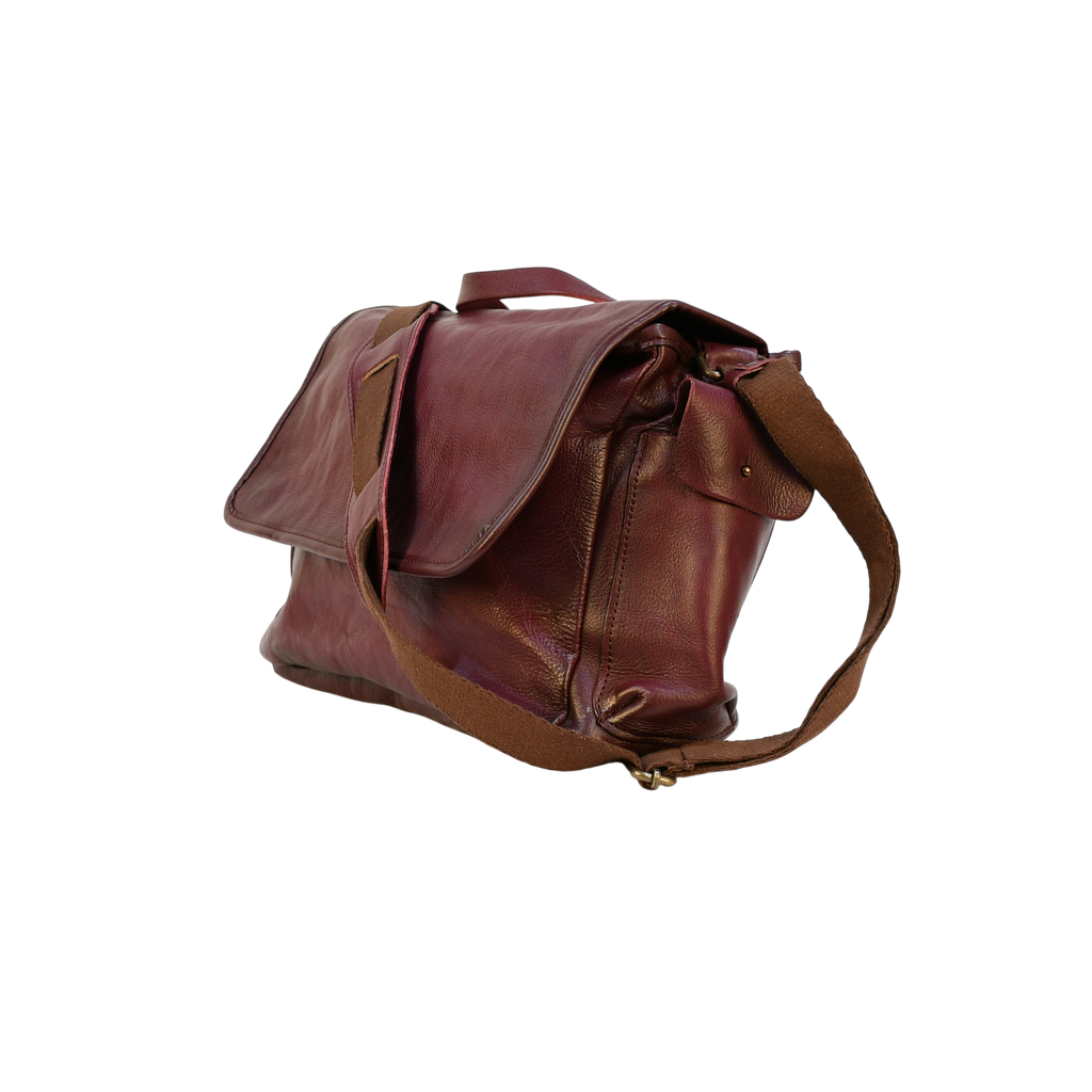 purple modern rugged leather bag on a wooden table with a bookshelf in the background