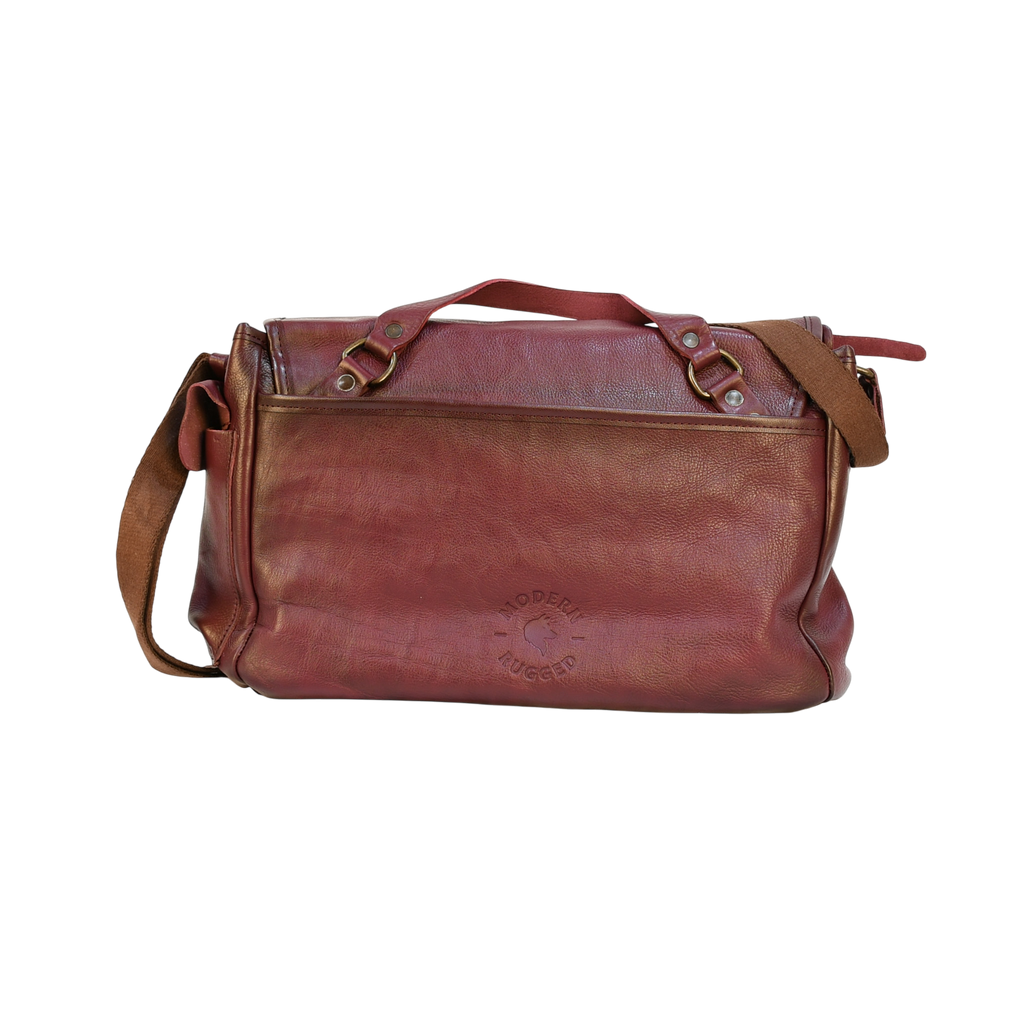 purple modern rugged leather bag on a wooden table with a bookshelf in the background