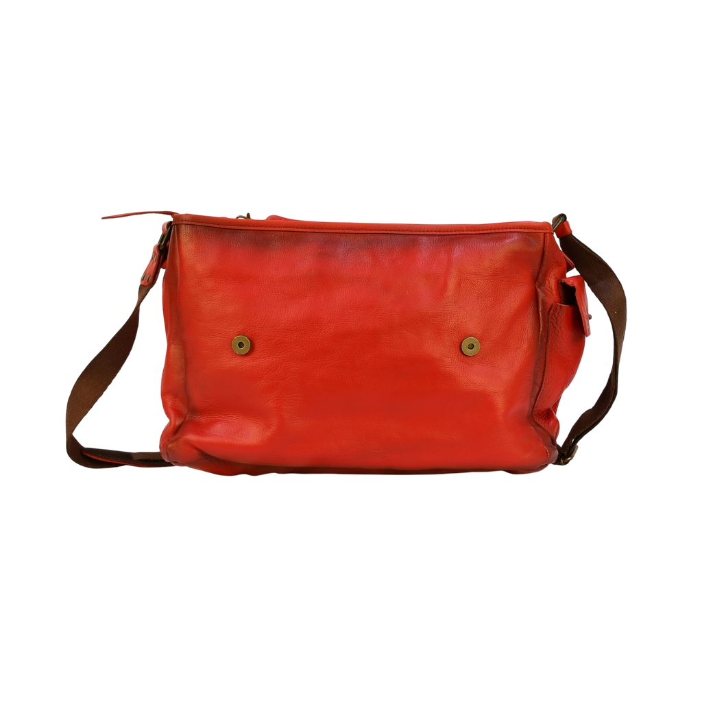 Red modern rugged leather bag on a wooden surface with books in the background