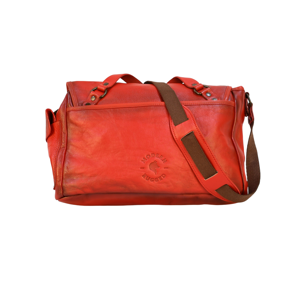 Red modern rugged leather bag on a wooden surface with books in the background