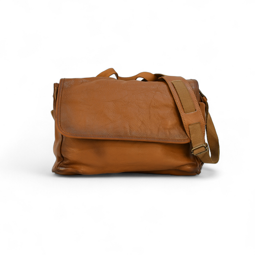 Brown leather modern rugged messenger bag on a surface with a window in the background