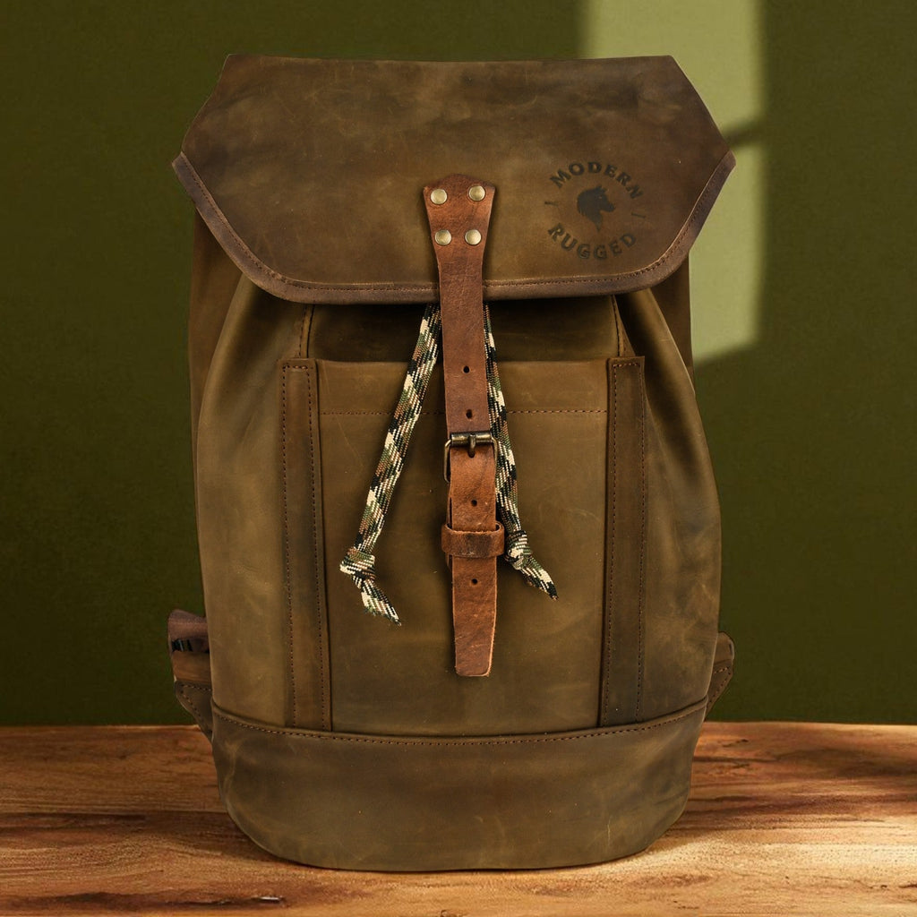 Olive leather backpack with a strap on a wooden surface against a green wall