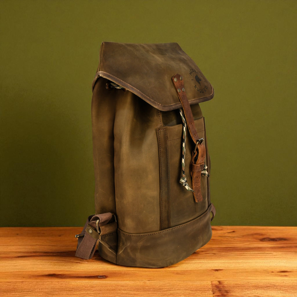 olive leather backpack on a wooden surface with a green background