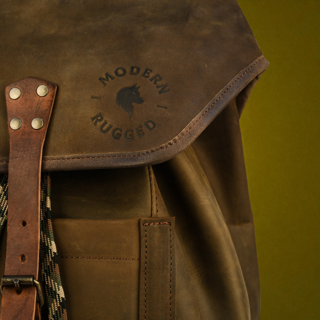 olive leather backpack with 'Modern Rugged' logo on a green background