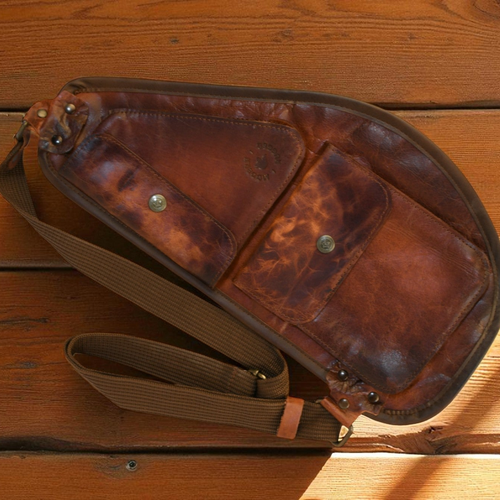 Brown leather slim sling bag with a strap on a wooden surface 