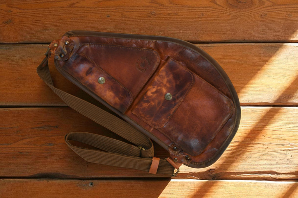 Brown leather slim sling bag with a strap on a wooden surface 