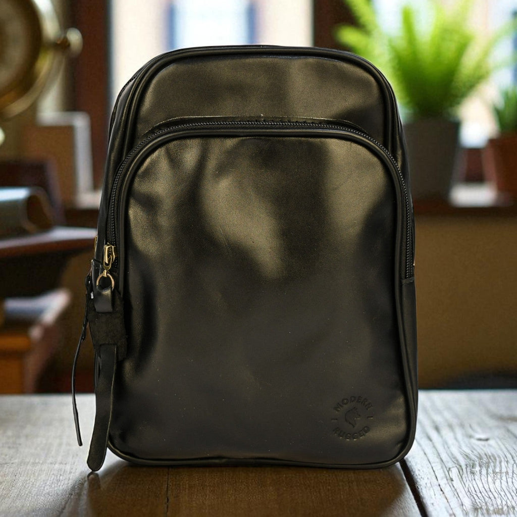 Black backpack leather sling bag on a wooden table with a blurred indoor background