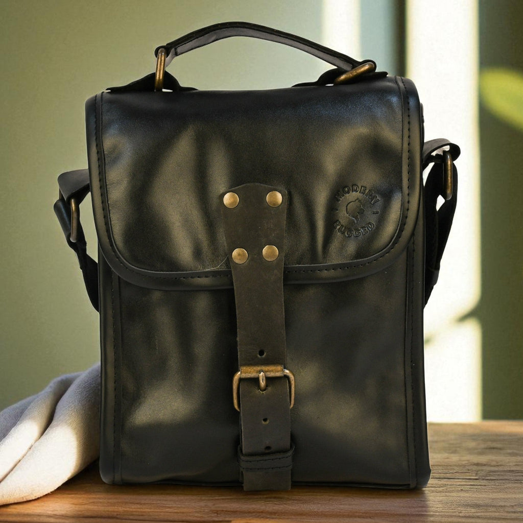 Black leather bag with brass buckles on a wooden surface with a blurred green background
