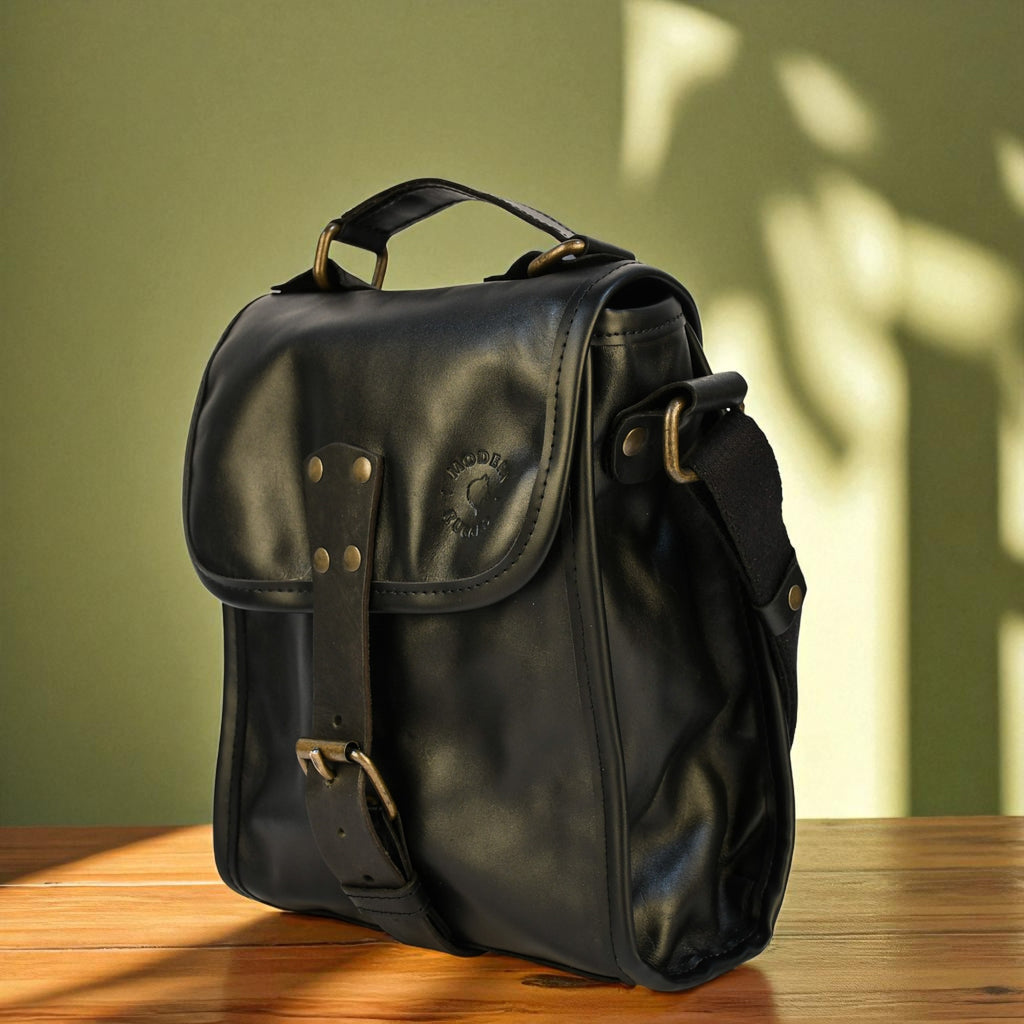 Black leather satchel bag on a wooden surface with a green wall background