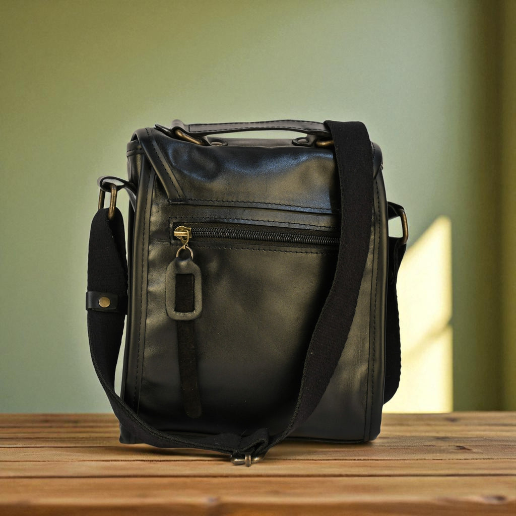 Black leather bag with a strap on a wooden surface against a green background